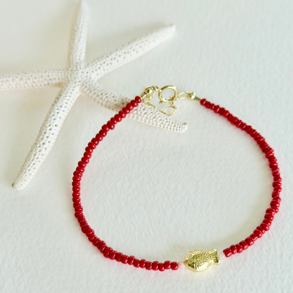 Red beaded bracelet with a gold clasp on a white background