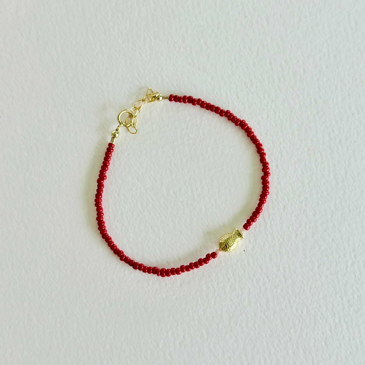 Red beaded bracelet with a gold clasp on a light gray background