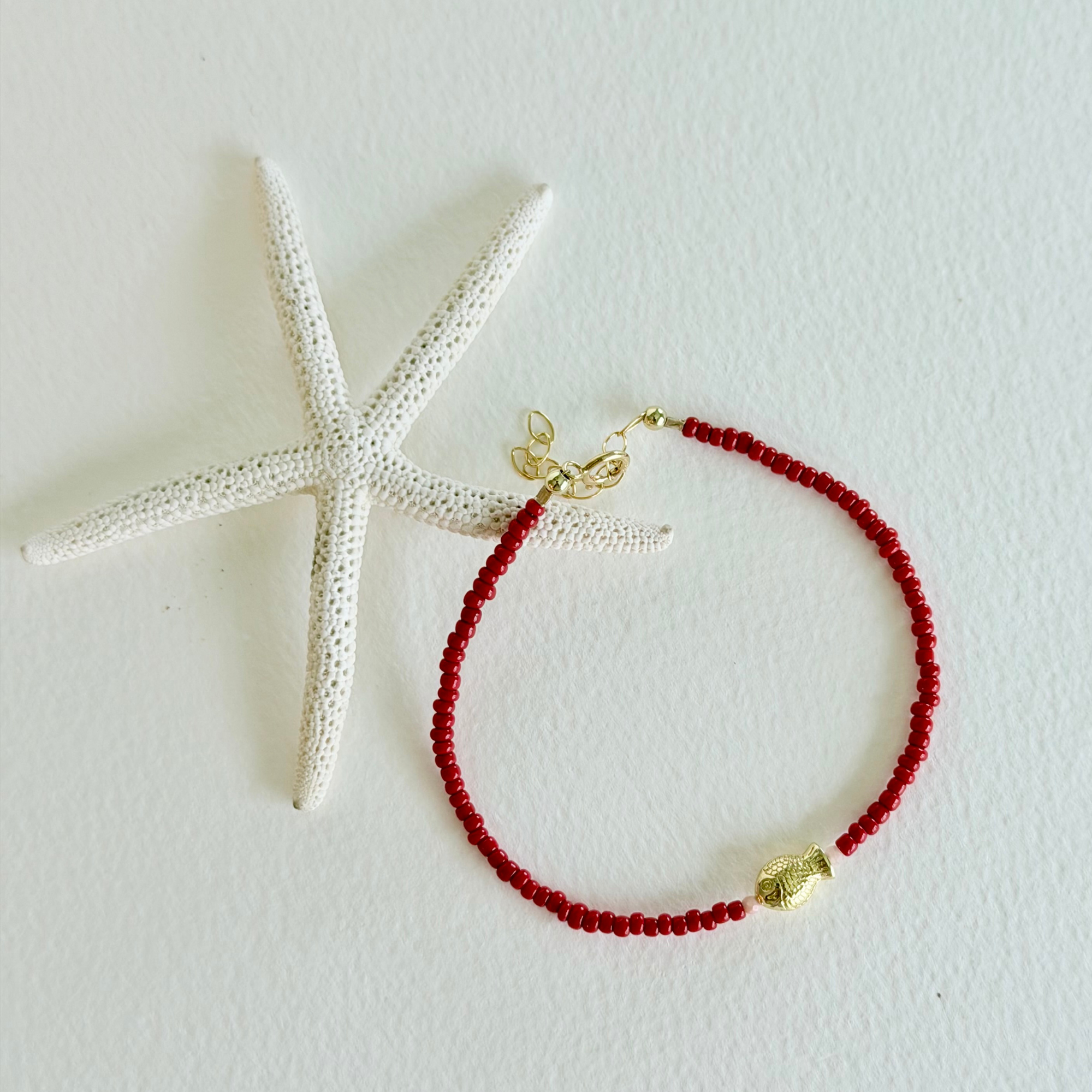 Red beaded bracelet with gold accents on a white background with a starfish.