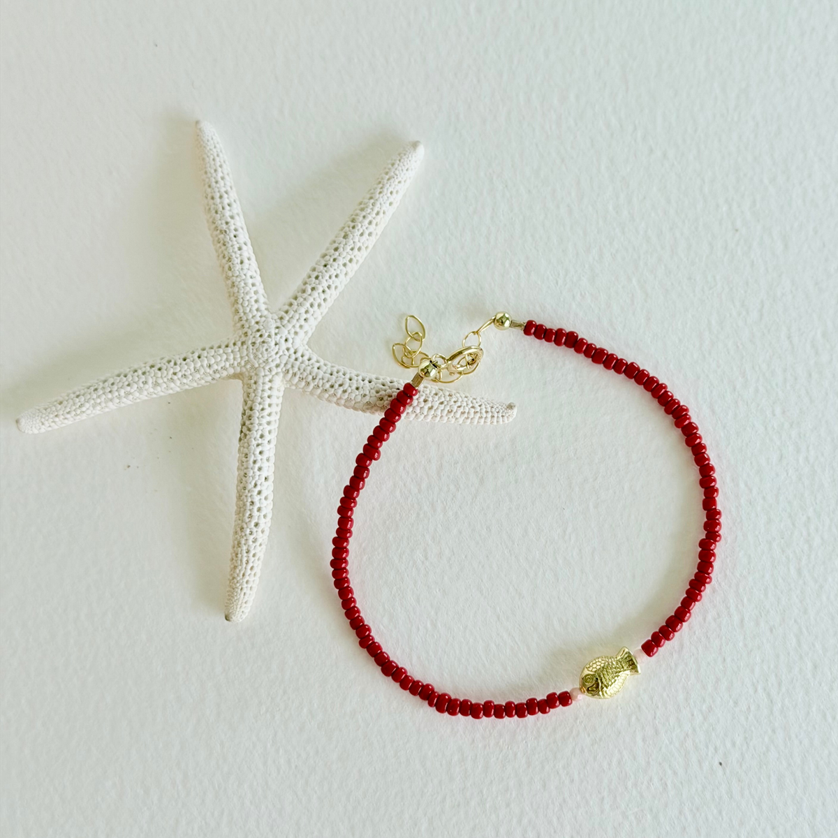 Red beaded bracelet with gold accents on a white background with a starfish.