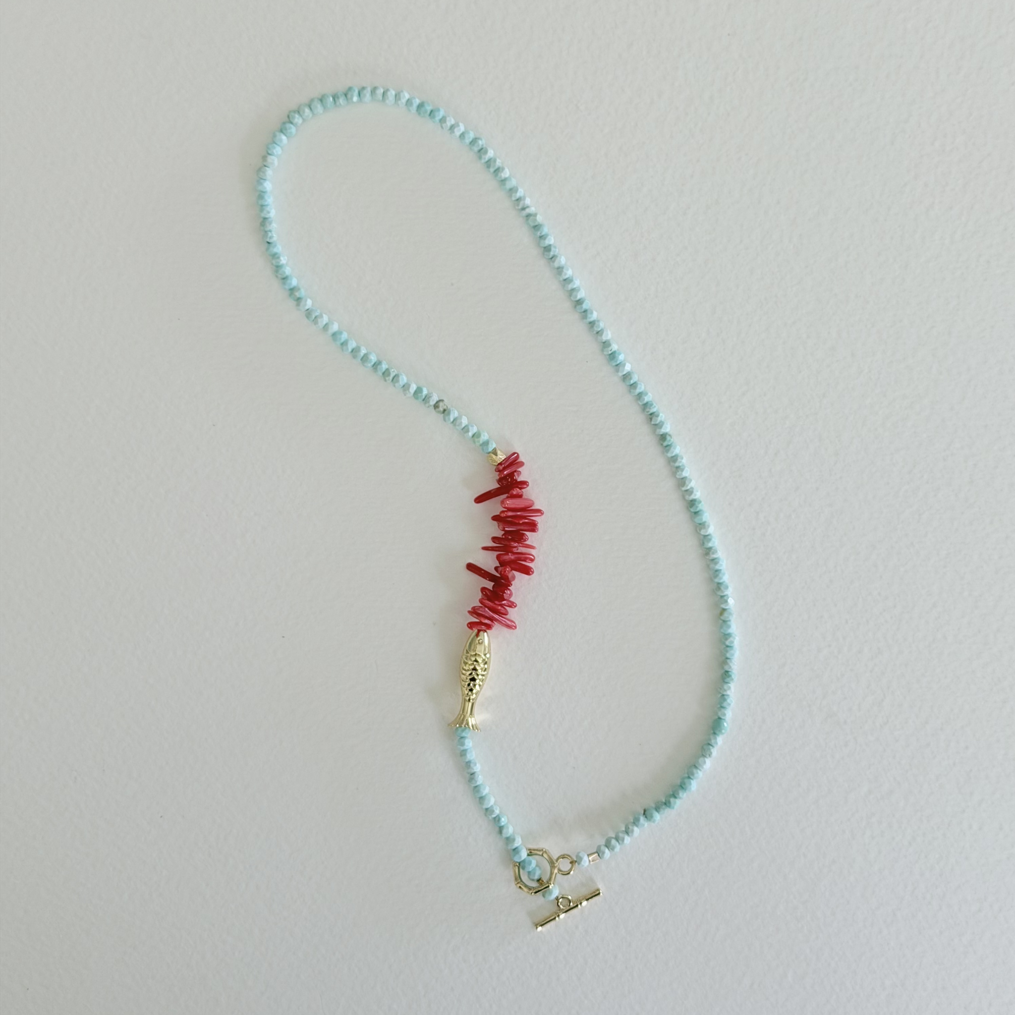 Handmade faceted aqua turquoise necklace with natural coral centerpiece, gold fish charm, and 14k gold-filled bamboo toggle clasp by Marie & Oakley.