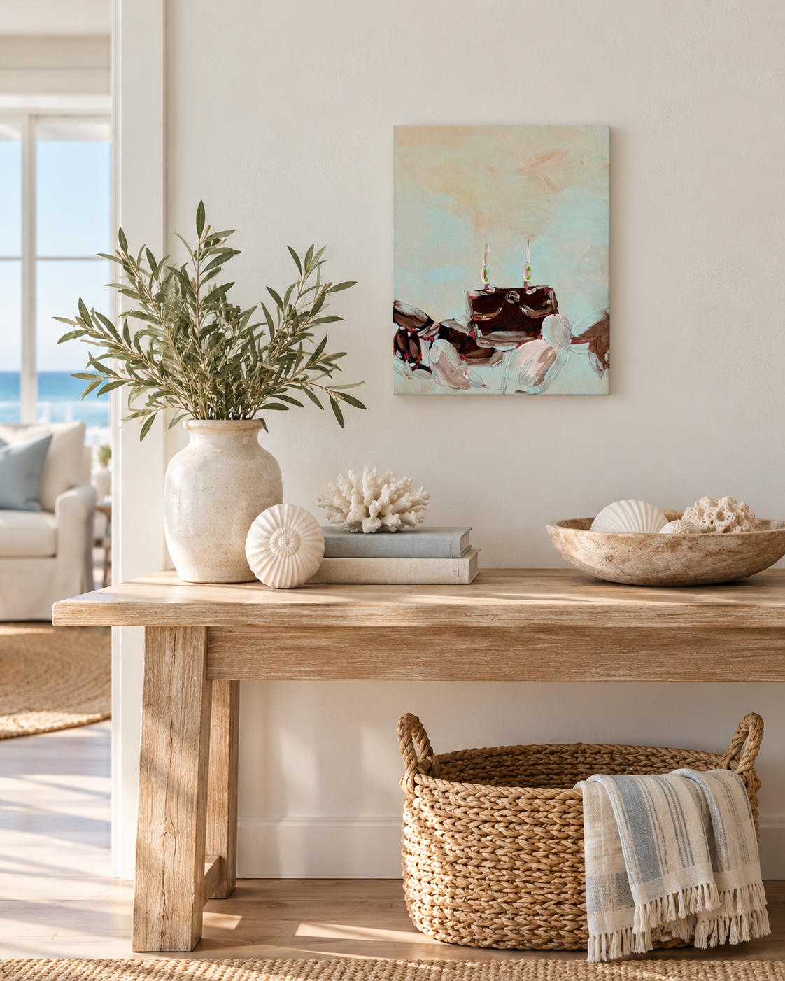 A coastal-style abstract canvas painting hangs on a white wall above a rustic wooden console table in a bright, modern living room. The painting features soft pastel blue, pink, and beige tones with dark brown abstract shapes intended to resemble a crab.