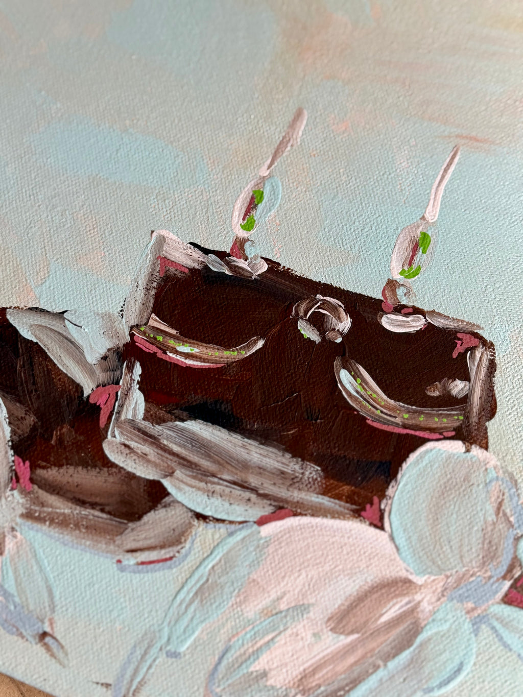 A close-up of an impressionistic painting depicting a dark brown rectangular cake or crab with two lit candles on top, surrounded by pale pink and white floral shapes against a soft light blue background.
