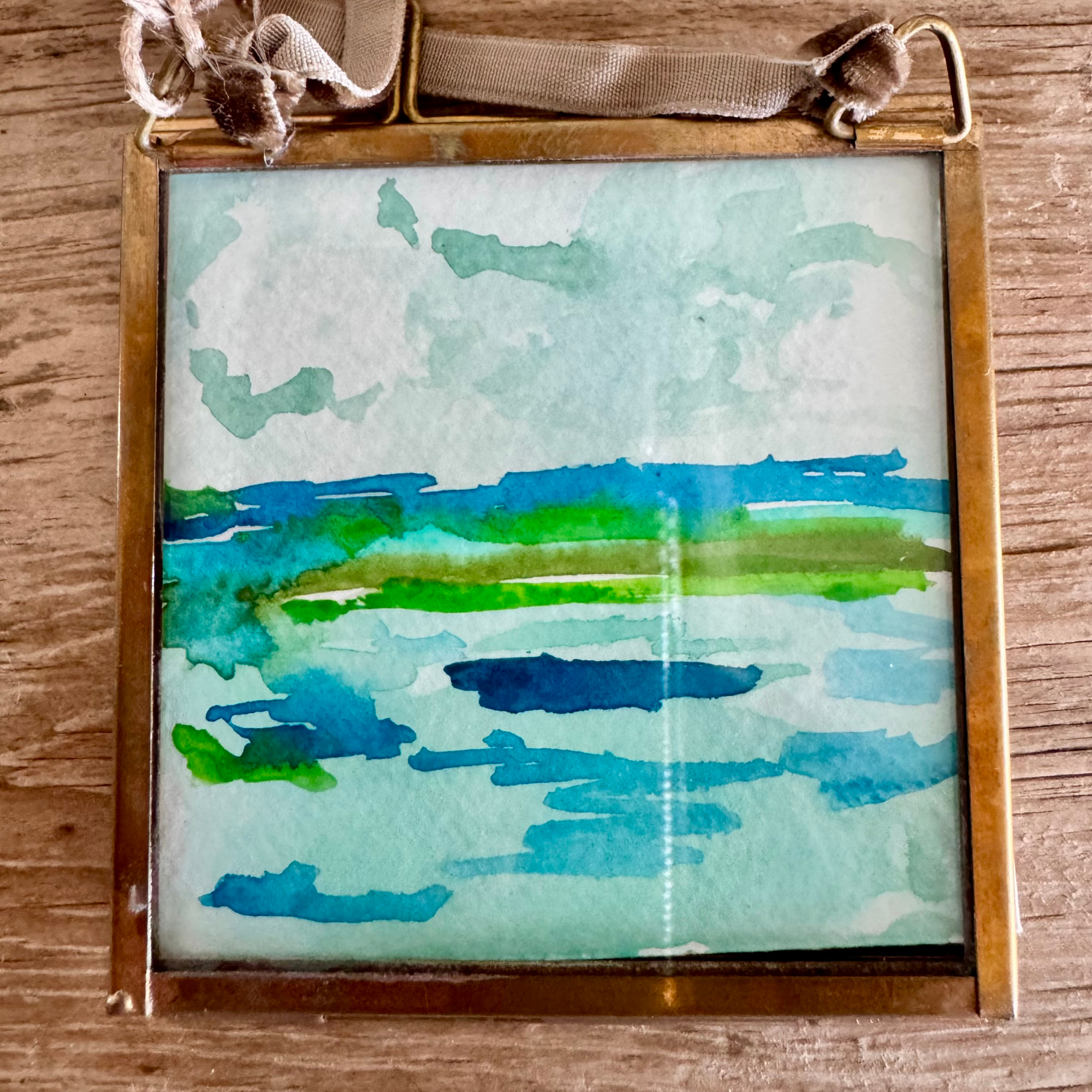 Watercolor of abstract seascape in blue and green. Framed in brass square glass frame and tied with brown velvet ribbon to hang as an ornament.