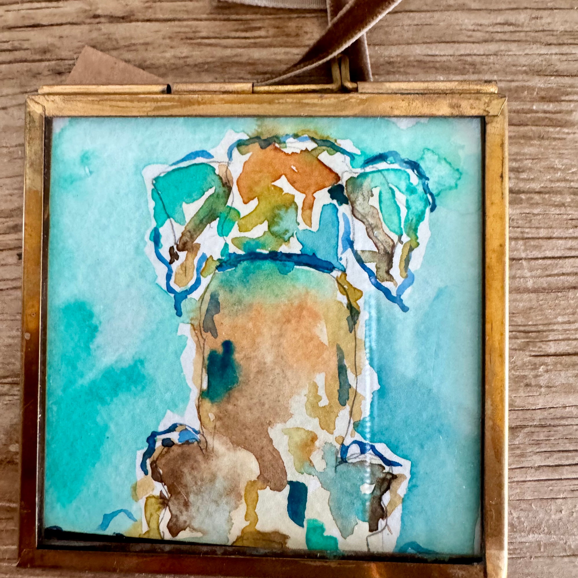Watercolor of dog in brown, blue, and gold. Framed in brass square glass frame and tied with brown velvet ribbon to hang as an ornament.