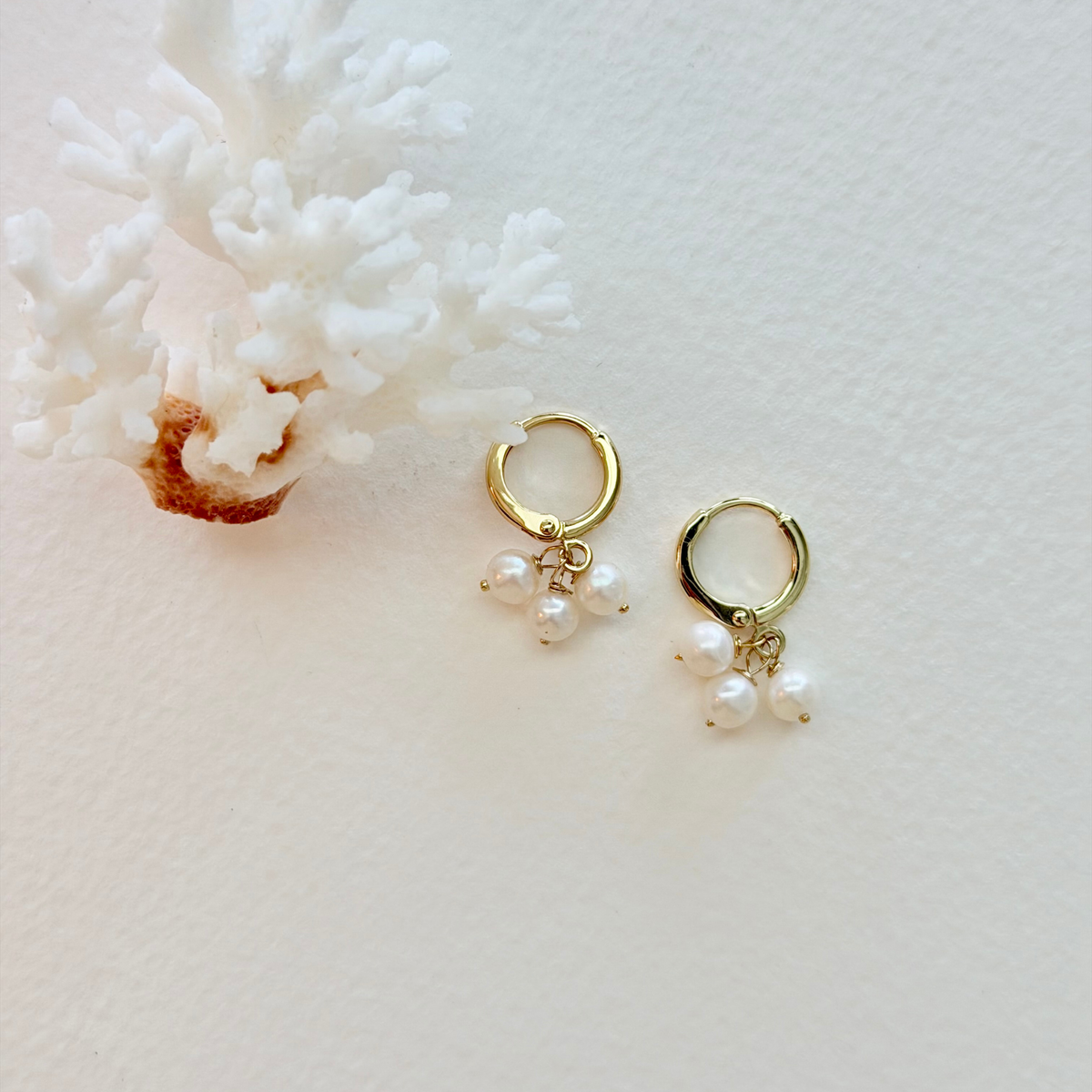 Gold hoop earrings with pearl drops on a white coral background