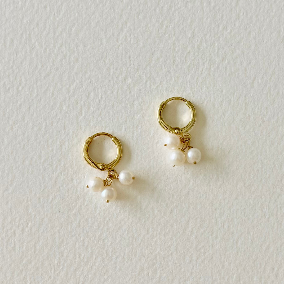 Gold hoop earrings with pearl charms on a light gray background