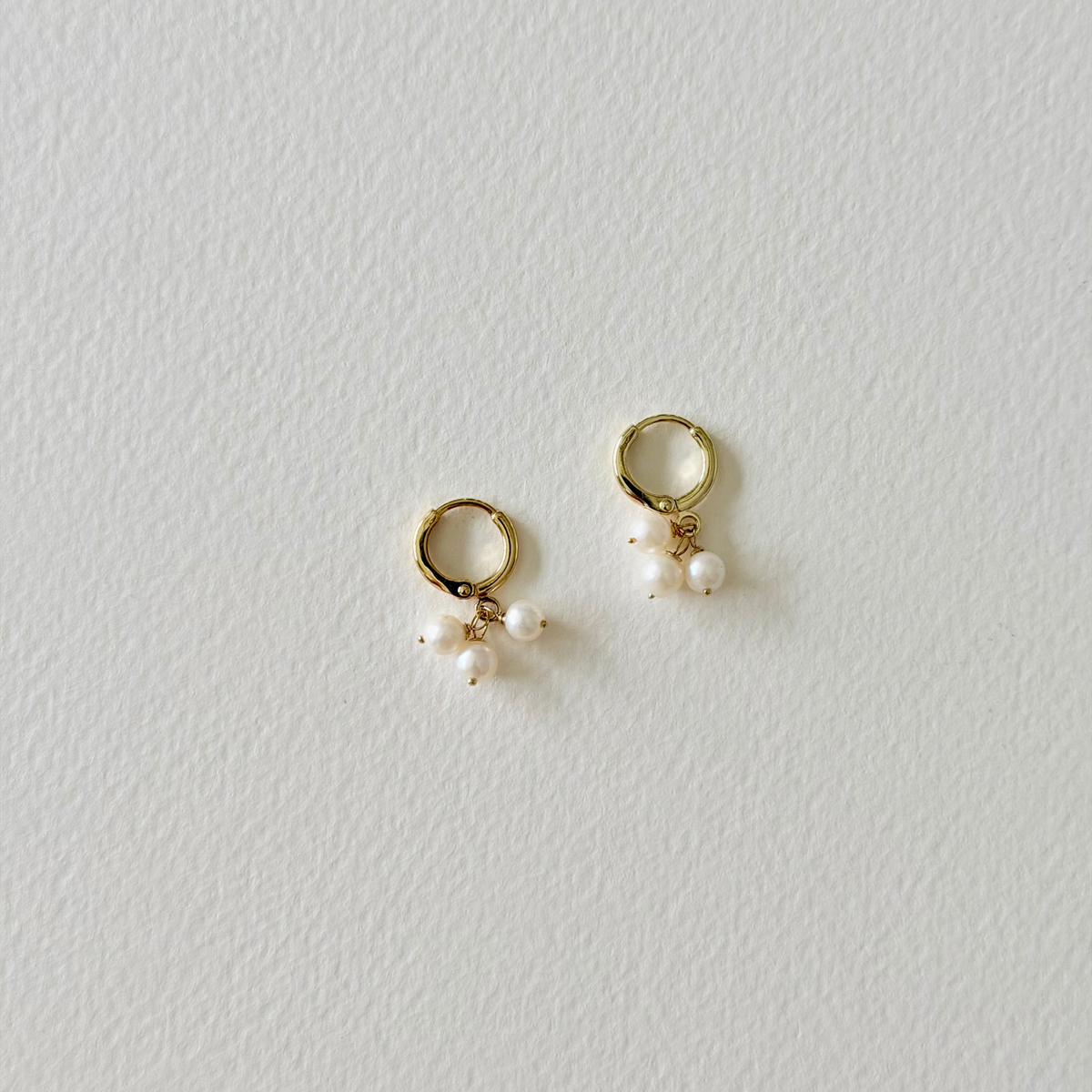 pearl gold huggie hoop earrings on light background