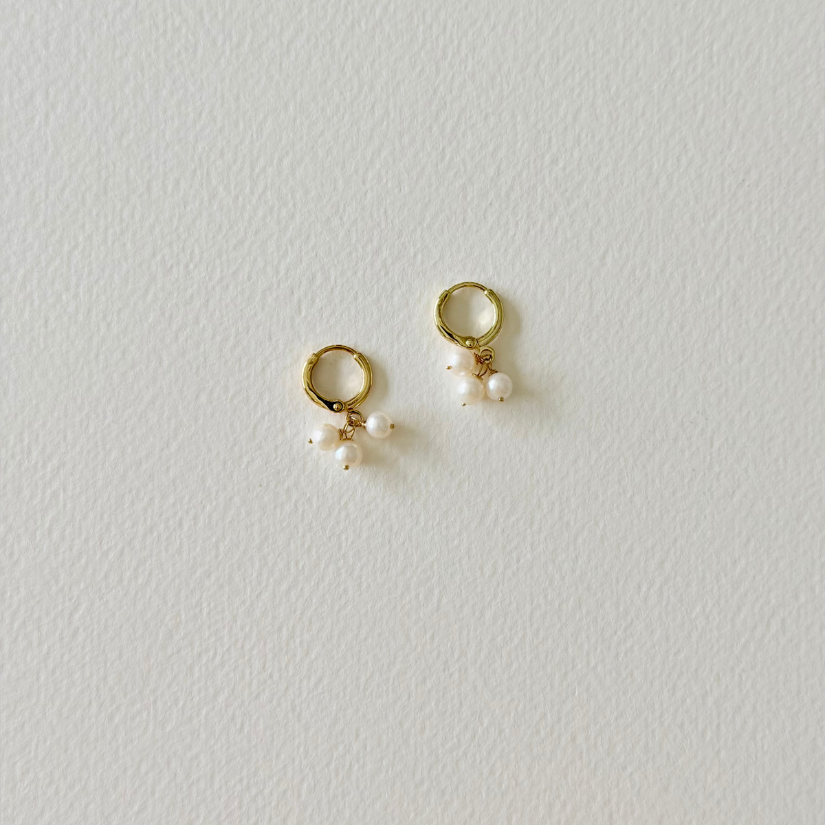 Pair of gold hoop earrings with small pearls on a light gray background