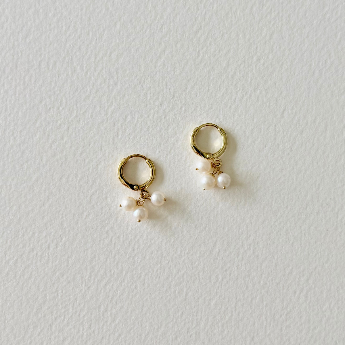 Gold hoop earrings with pearl drops on a light gray background
