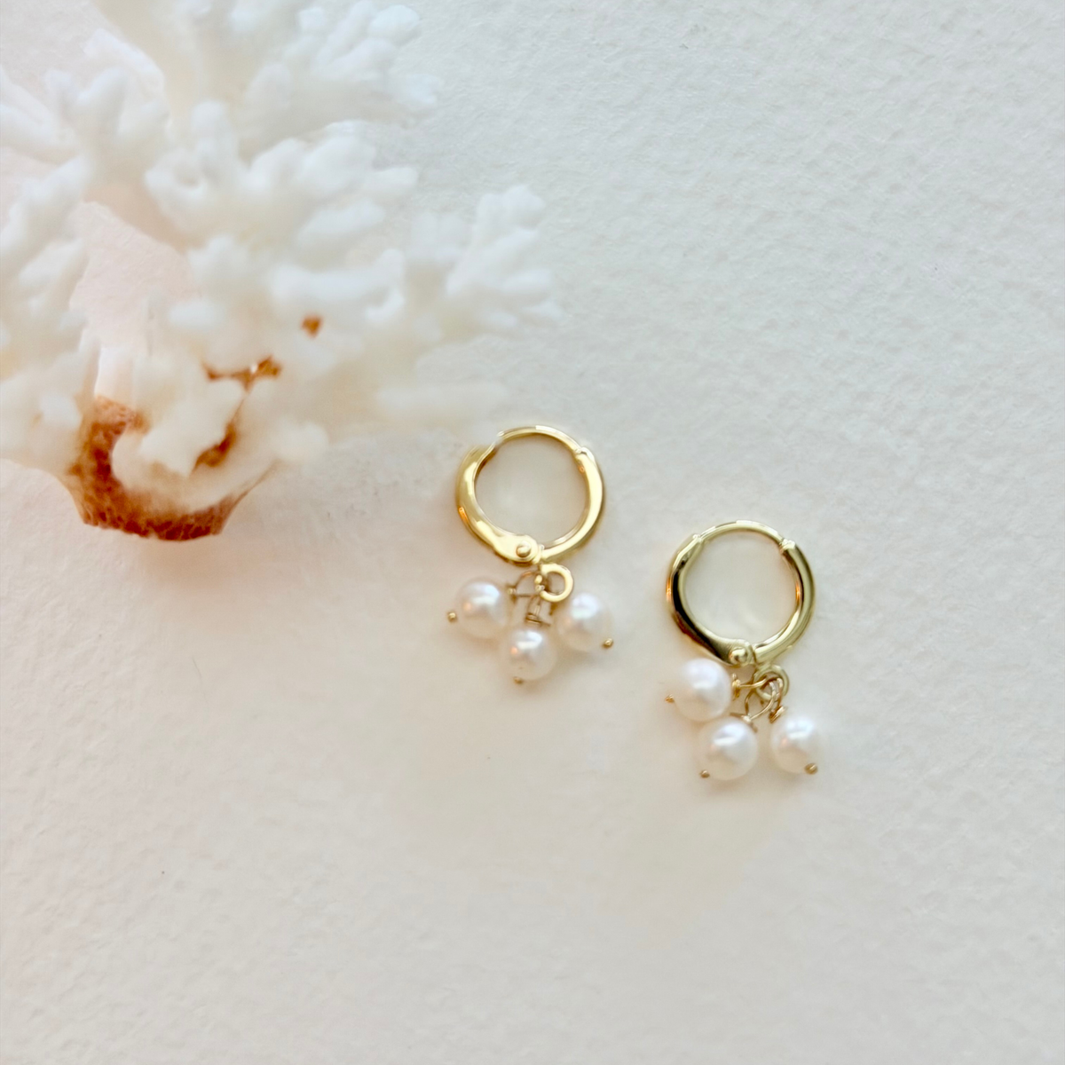 Gold hoop earrings with pearl drops on a light background
