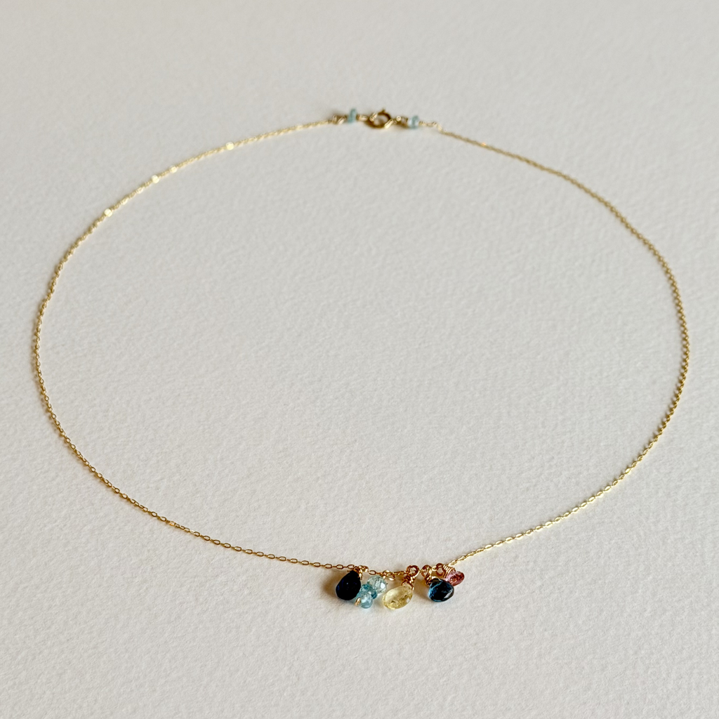 Gold necklace with colorful gemstones on a light gray background