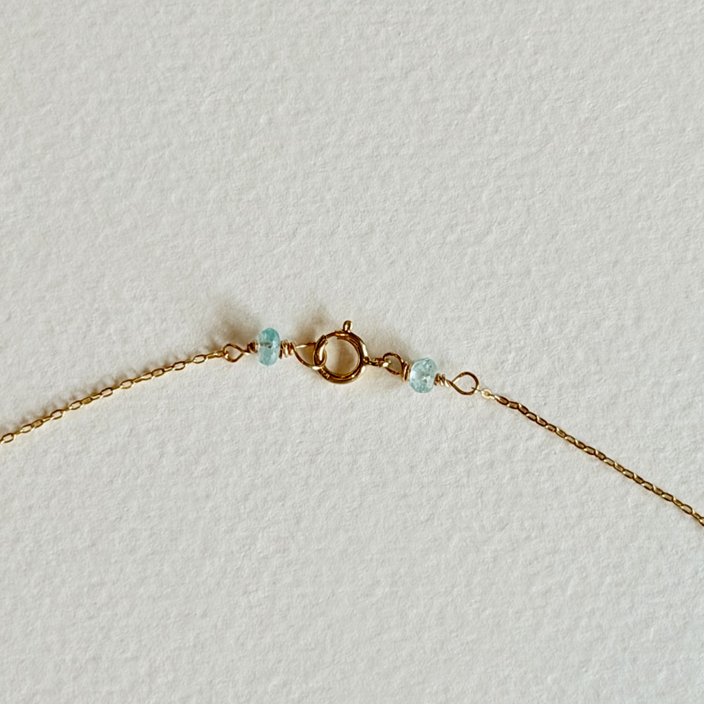 Gold necklace with small turquoise beads on a light gray background
