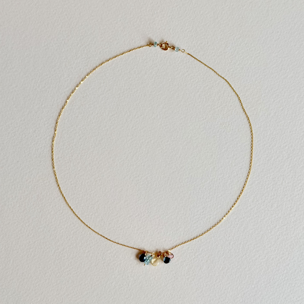 Gold necklace with small multicolored beads on a light gray background