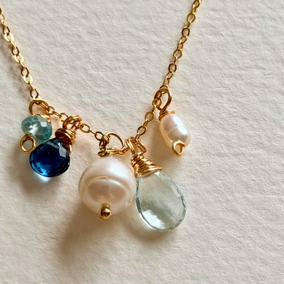 Necklace with gold chain, blue, pearls, and aquamarine beads on a light background