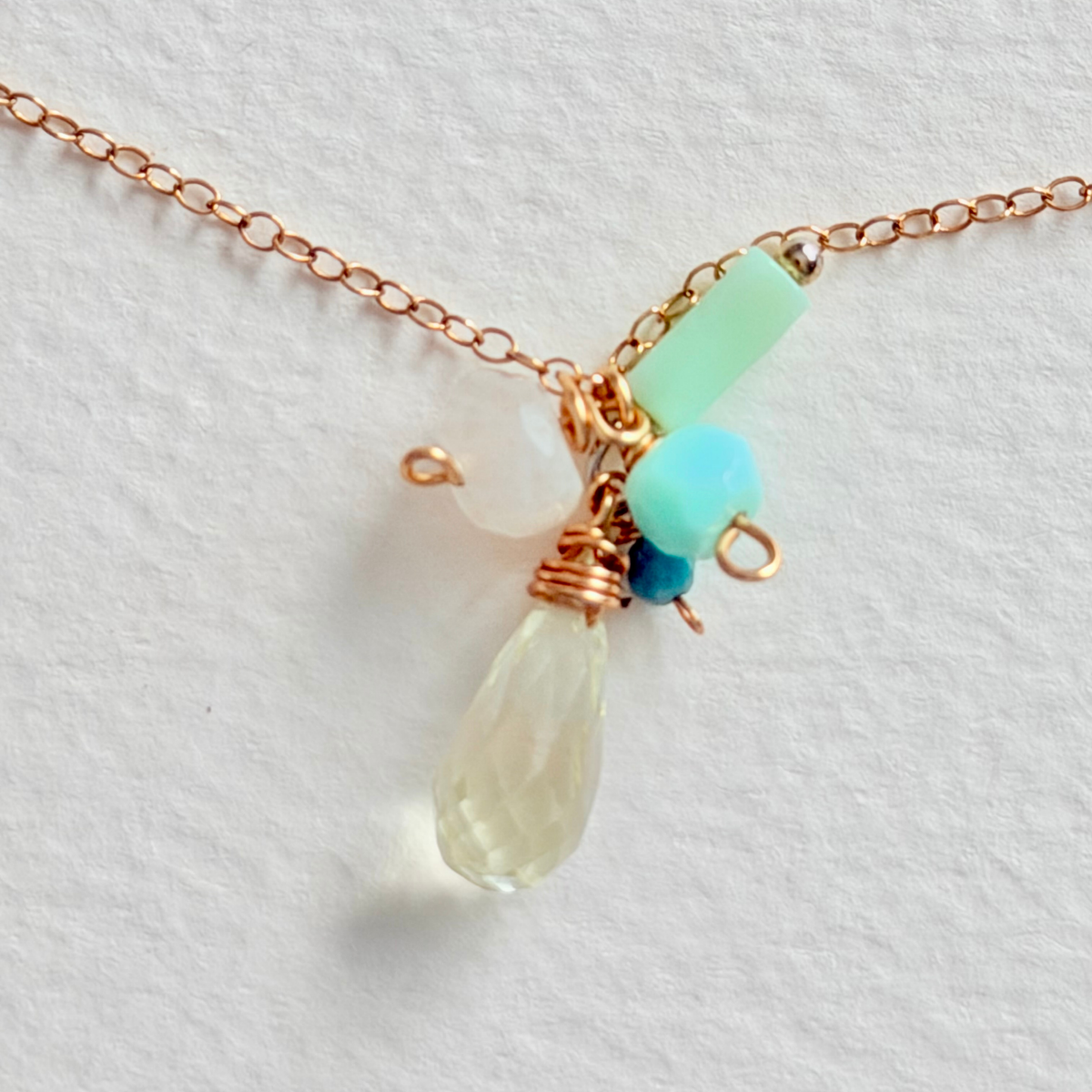 Necklace with teardrop-shaped pendant and green and blue beads on a light background