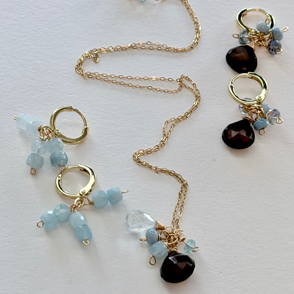 Gold necklace with blue and black beaded charms on a white background styled with huggie earrings