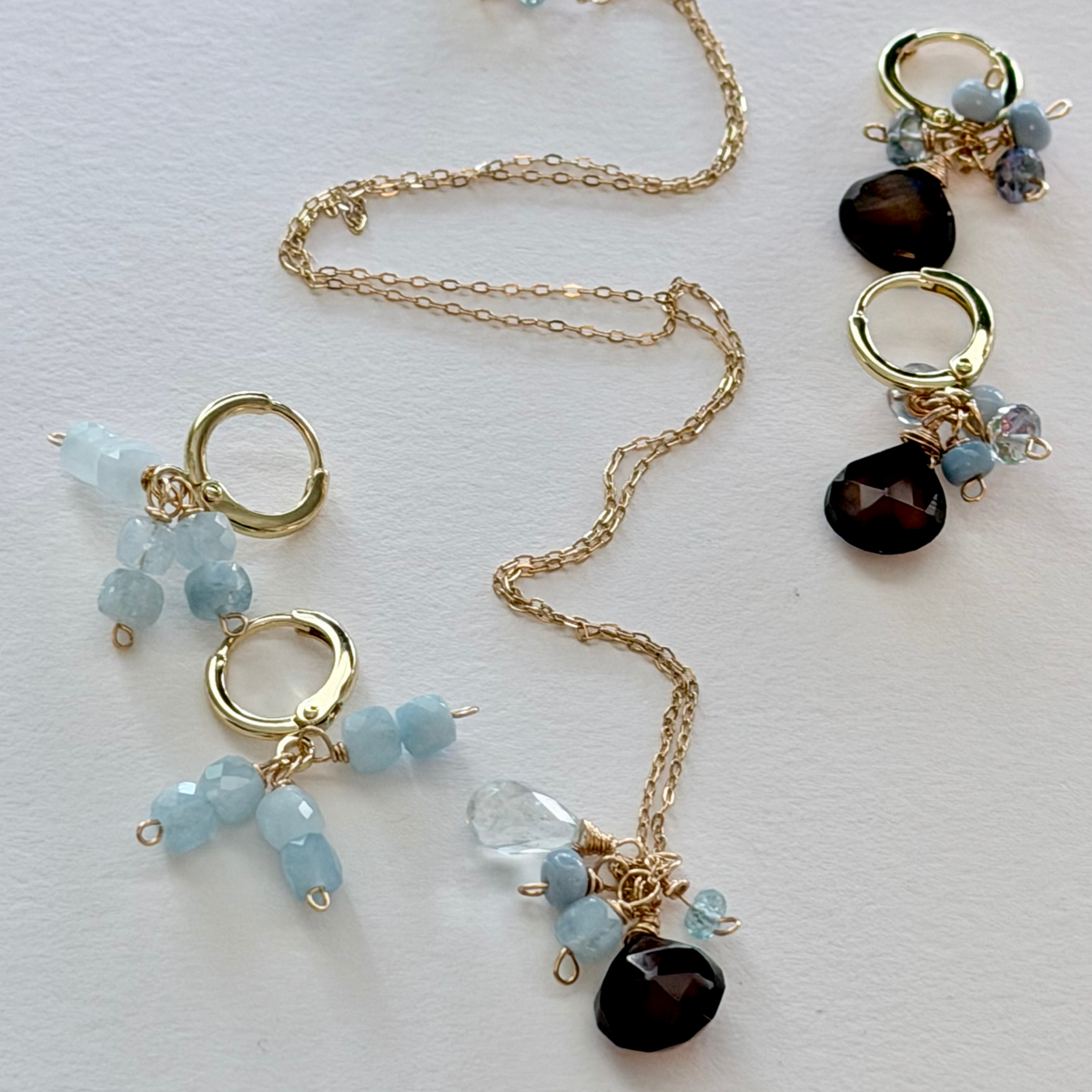 Gold necklace with blue and black beaded charms on a white background styled with huggie earrings