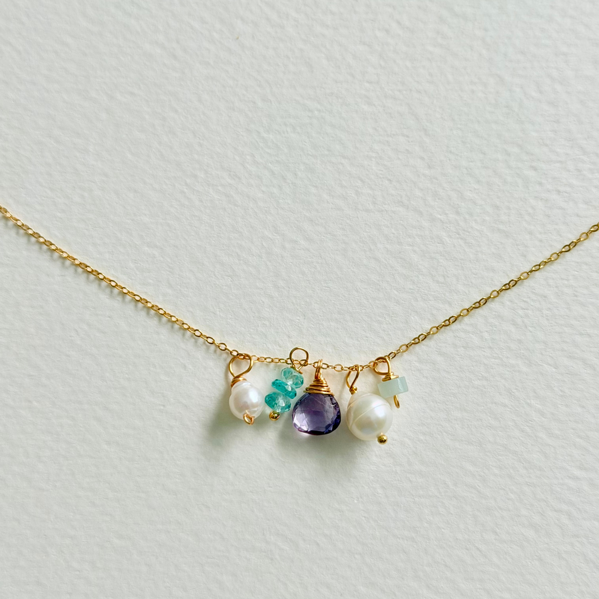 Necklace with pearls, amethyst, and turquoise stones on a light gray background