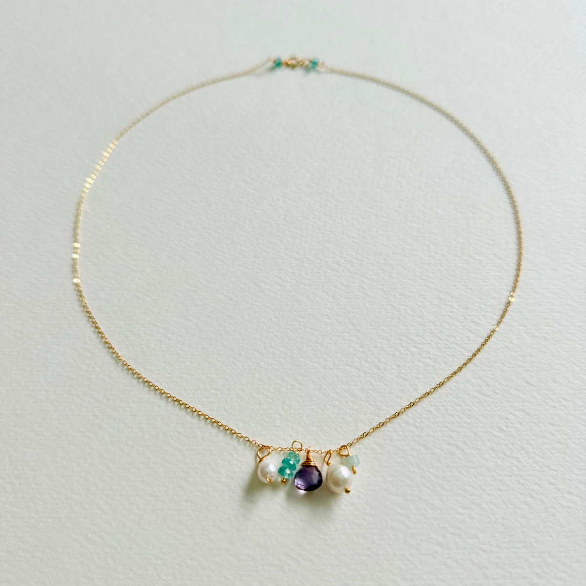 Delicate gold necklace with gemstones on a light gray background