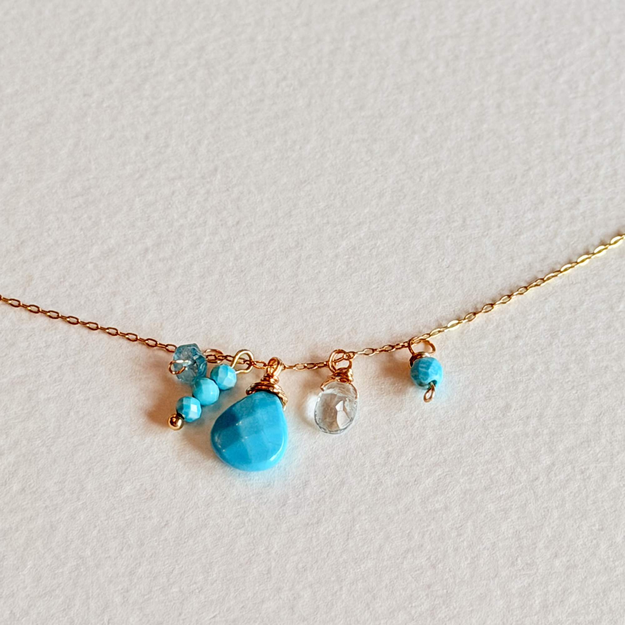 Necklace with blue beads and gold chain on a light gray background