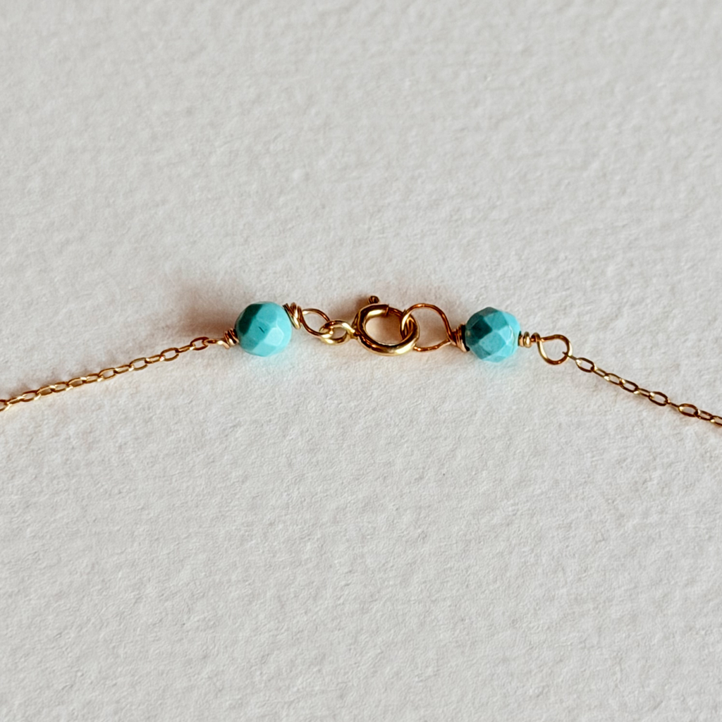 Gold bracelet with turquoise beads on a light gray background