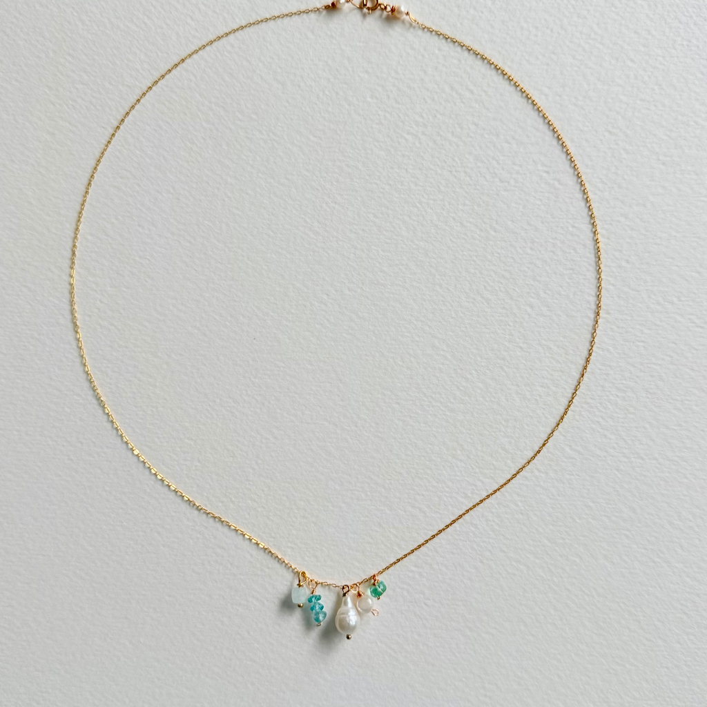 Delicate gold necklace with pearls and green gemstones on a light gray background