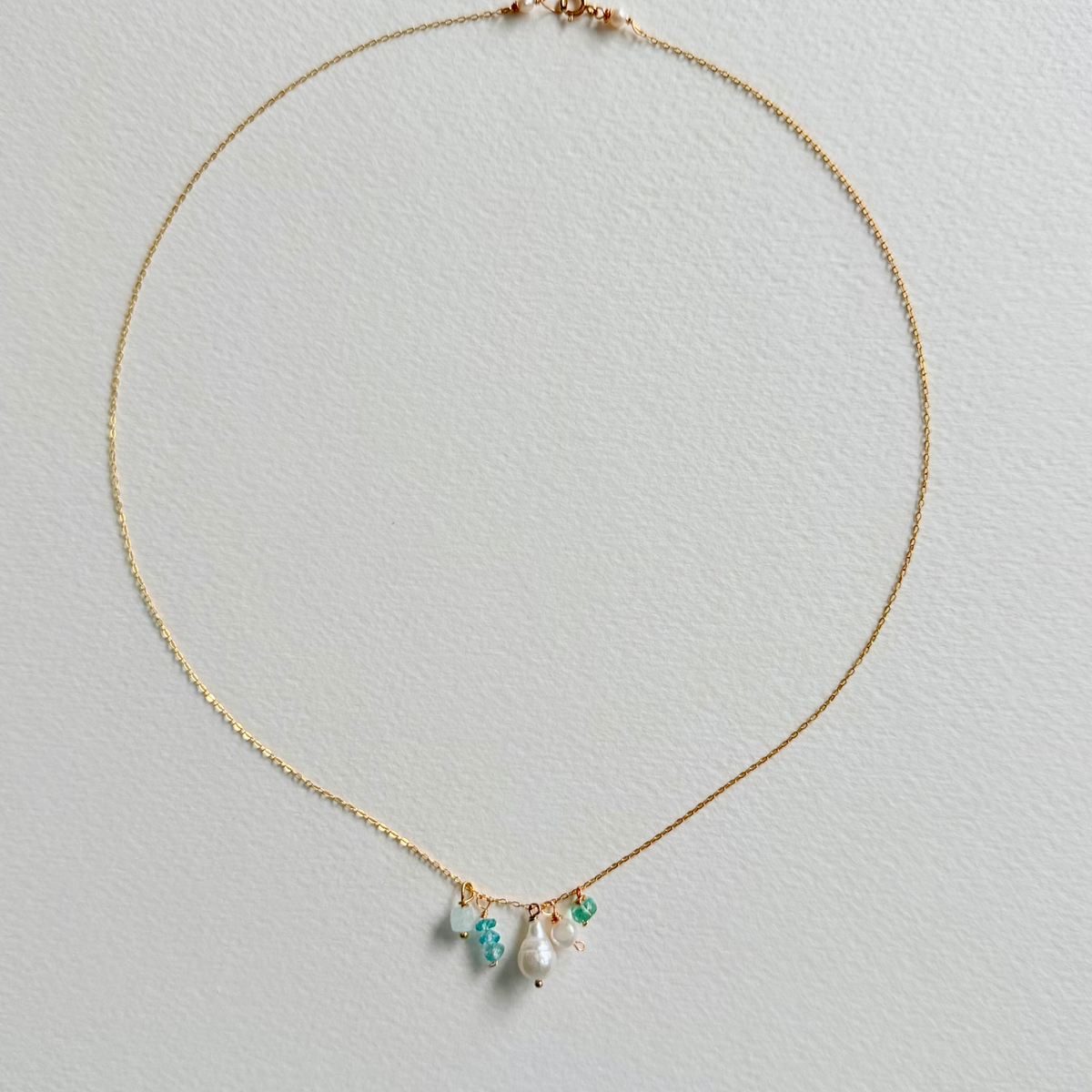 Delicate gold necklace with pearls and green gemstones on a light gray background