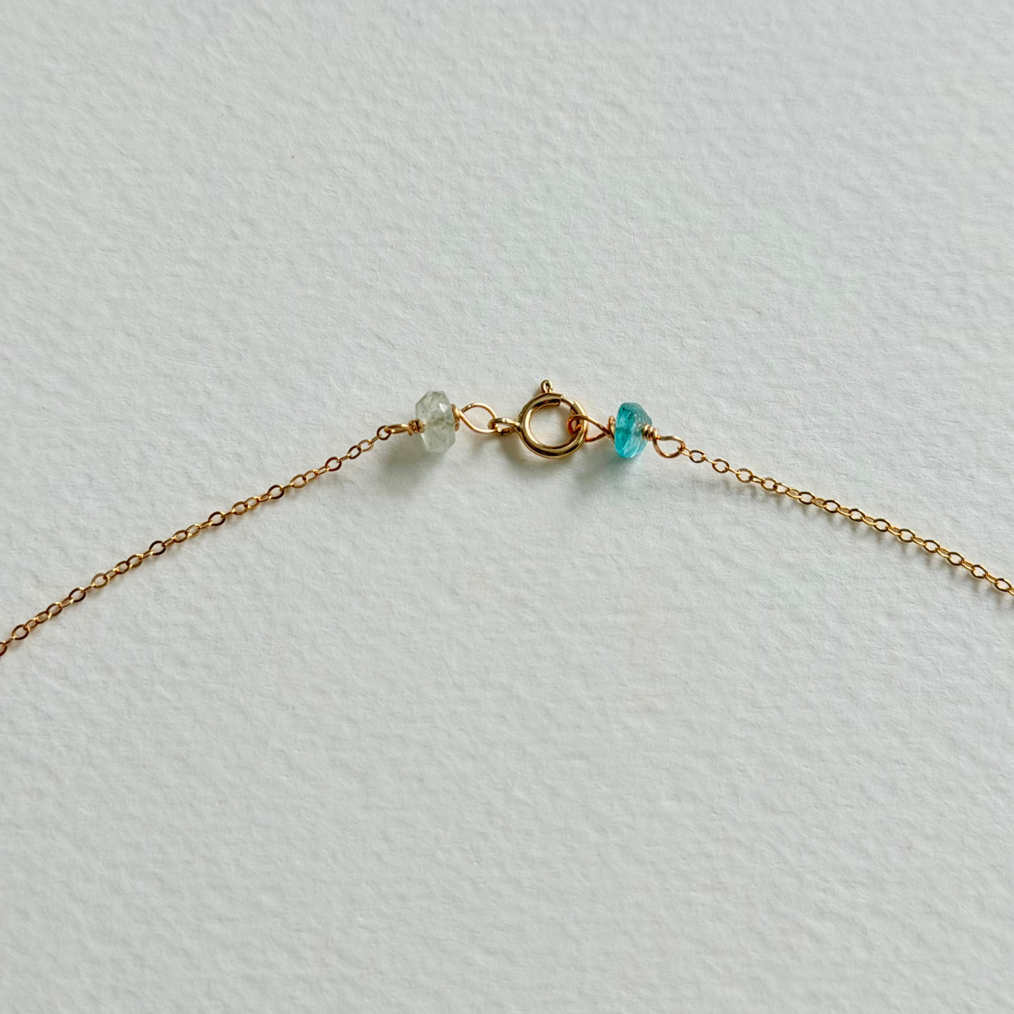 Gold necklace with turquoise bead on a light gray background