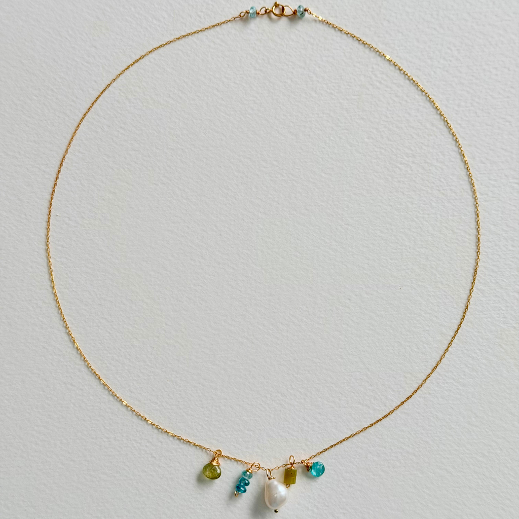 Delicate gold necklace with colorful beads on a light gray background