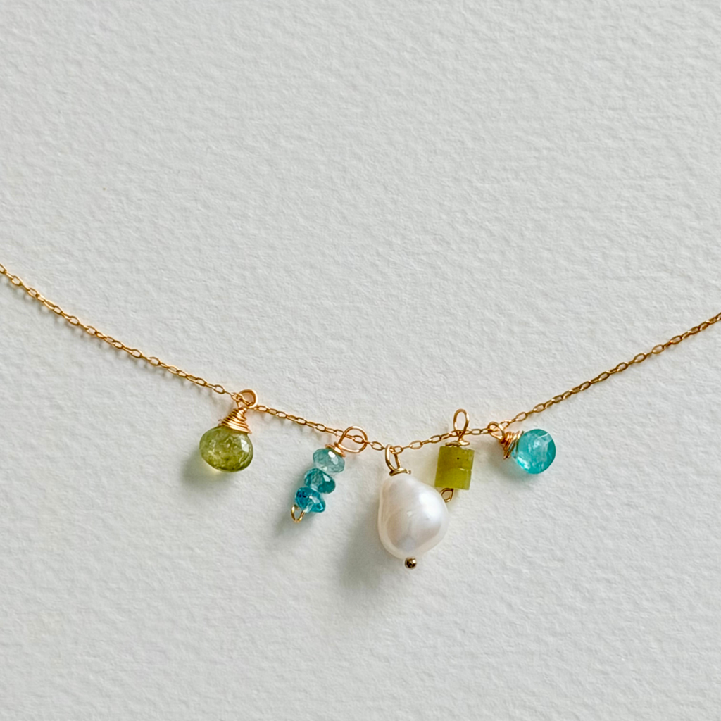 Necklace with green and blue beads and a pearl on a light gray background
