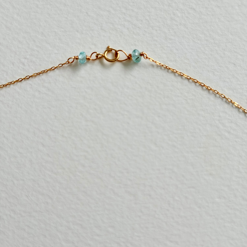 Gold chain necklace with small blue beads on a light gray background