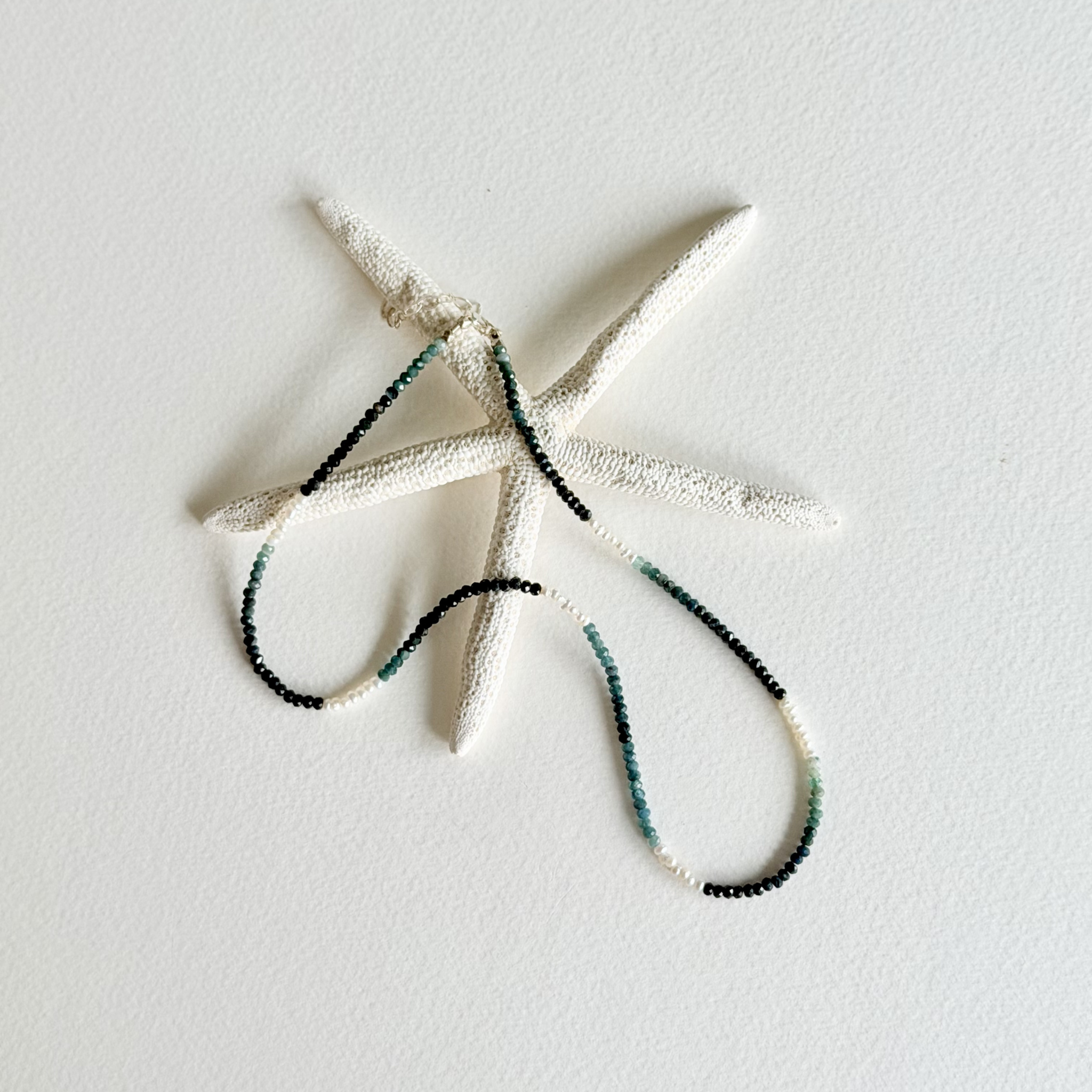 A white starfish-shaped wall hanging with a beaded necklace draped across it, set against a plain white textured background.