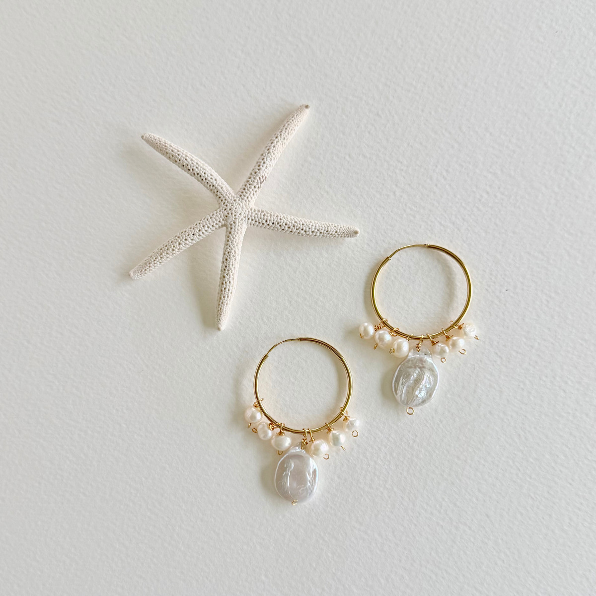 Gold hoop earrings with pearls and clear stones on a light gray background with a starfish.