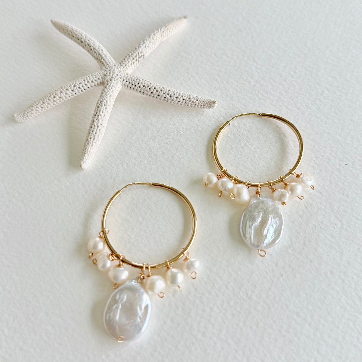 Gold hoop earrings with pearls and large beads on a light background with a starfish.