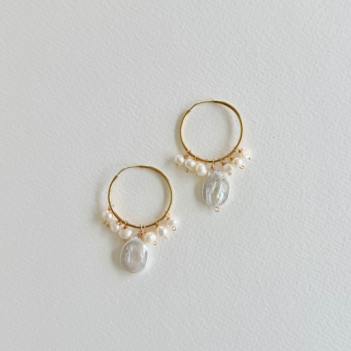 Gold hoop earrings with pearl drops on a light gray background