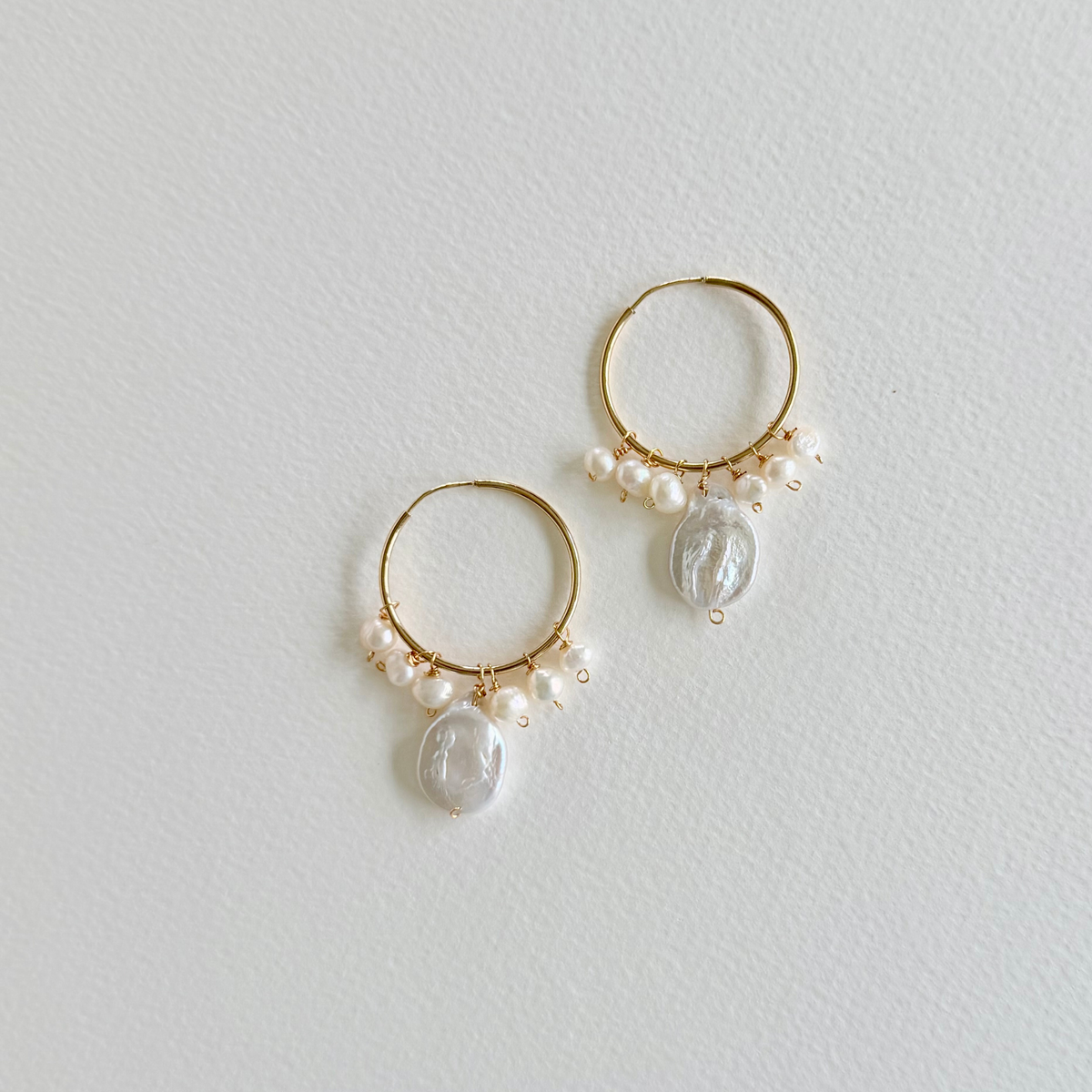 Gold hoop earrings with pearl and crystal drops on a light gray background