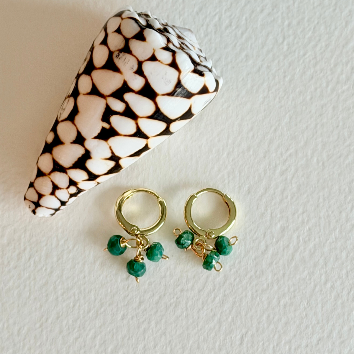 Gold hoop earrings with green beads on a textured white surface