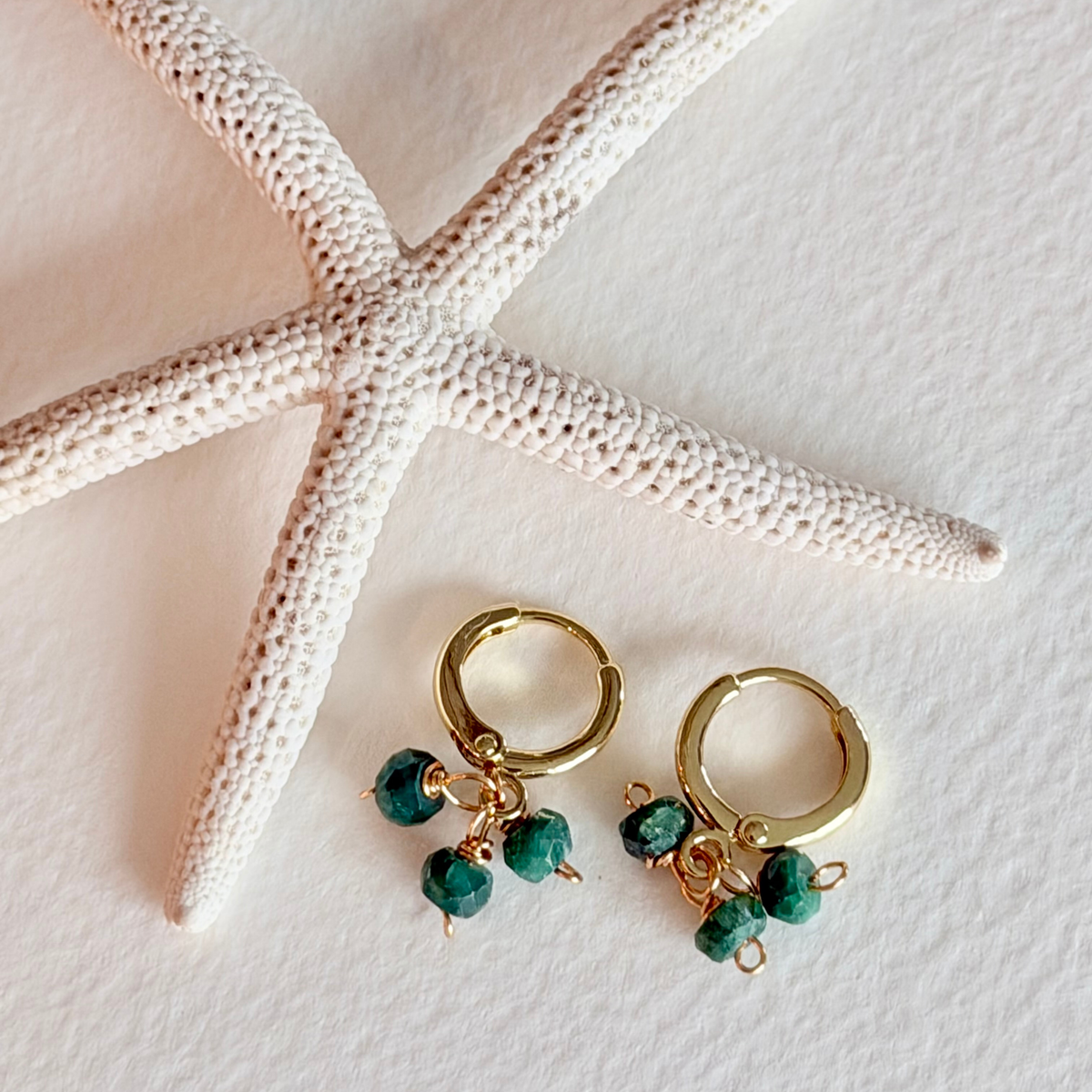 Gold hoop earrings with green beads on a white surface with a starfish.