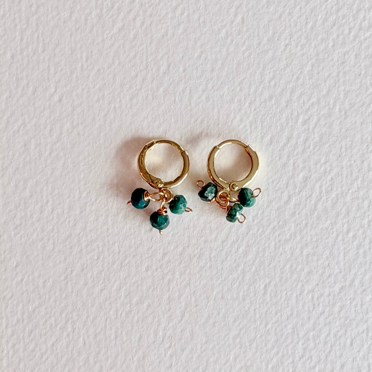Gold hoop earrings with green beads on a light gray background