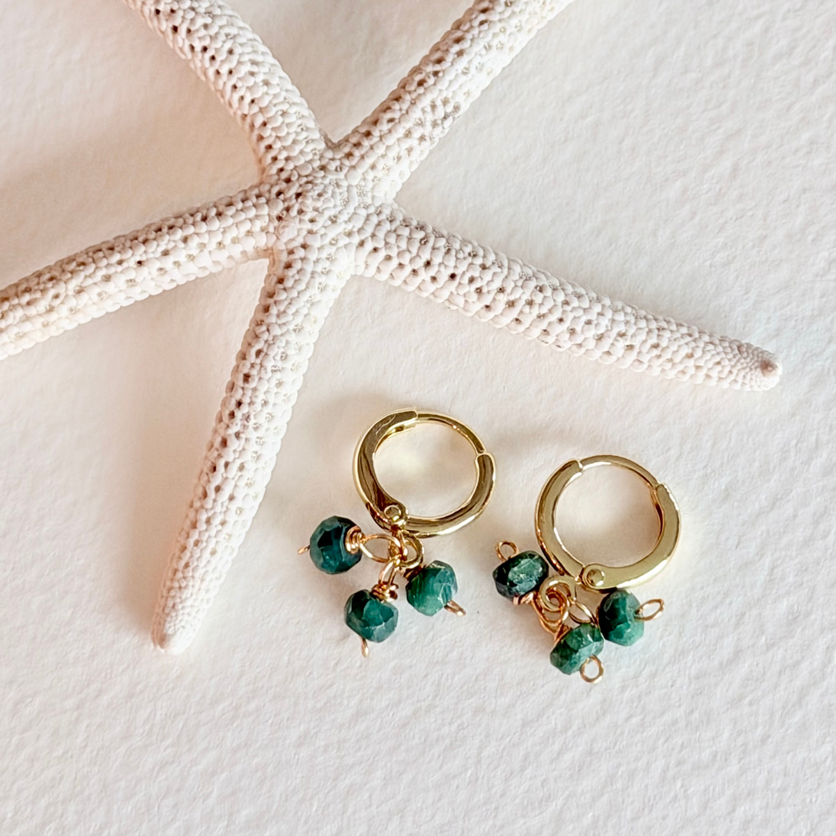 Gold hoop earrings with green beads on a white surface with a starfish.