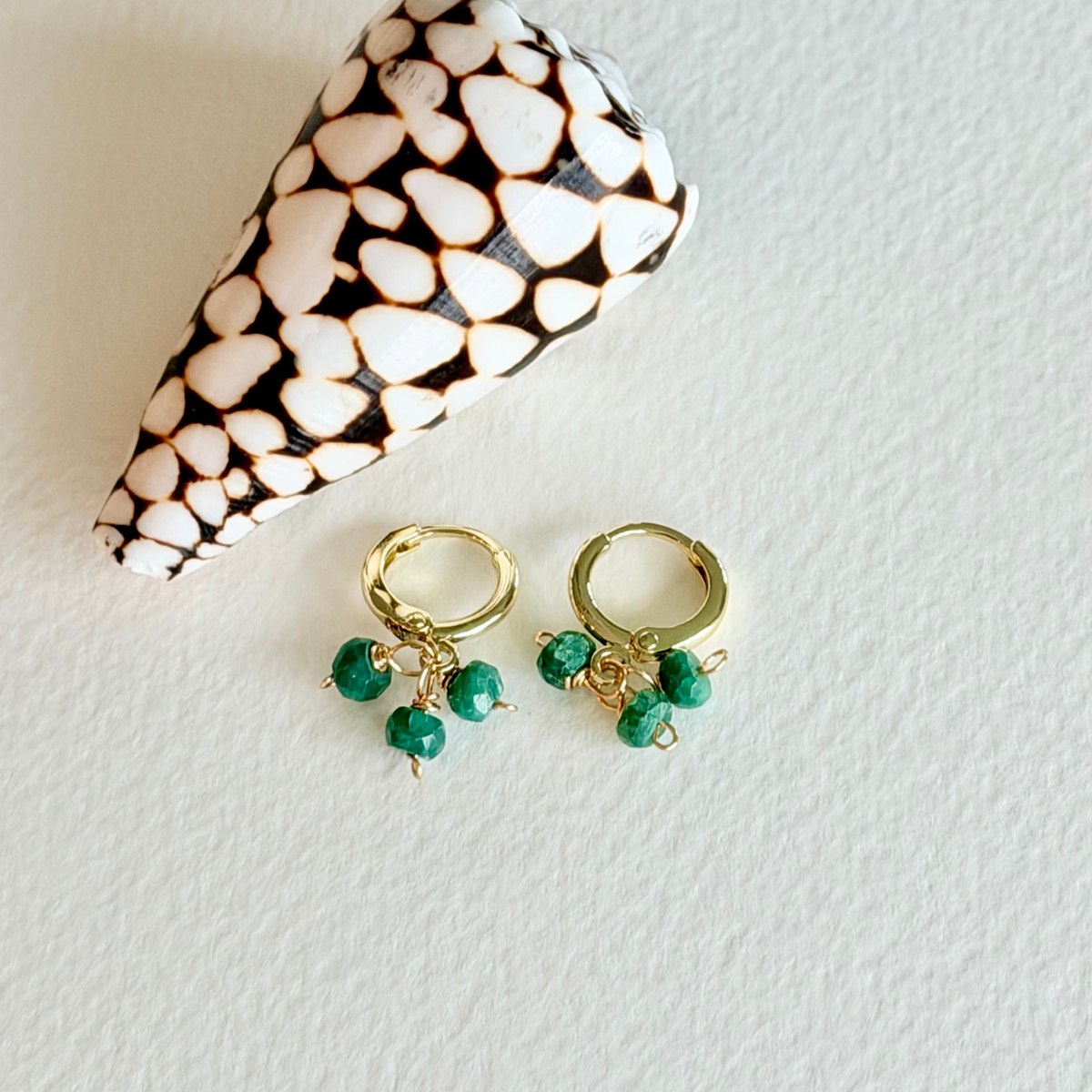 Gold hoop earrings with green beads on a textured white surface.