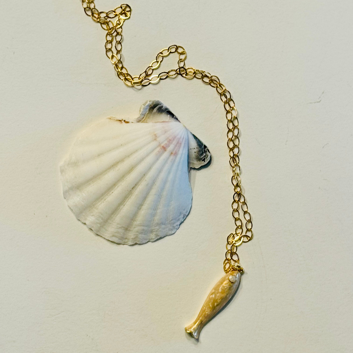 Necklace with a shell and fish pendant on a light gray background