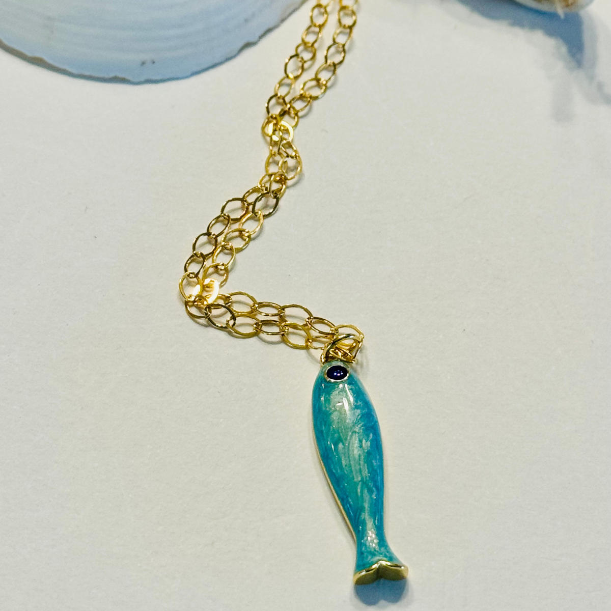 Gold chain necklace with a blue fish pendant on a light background