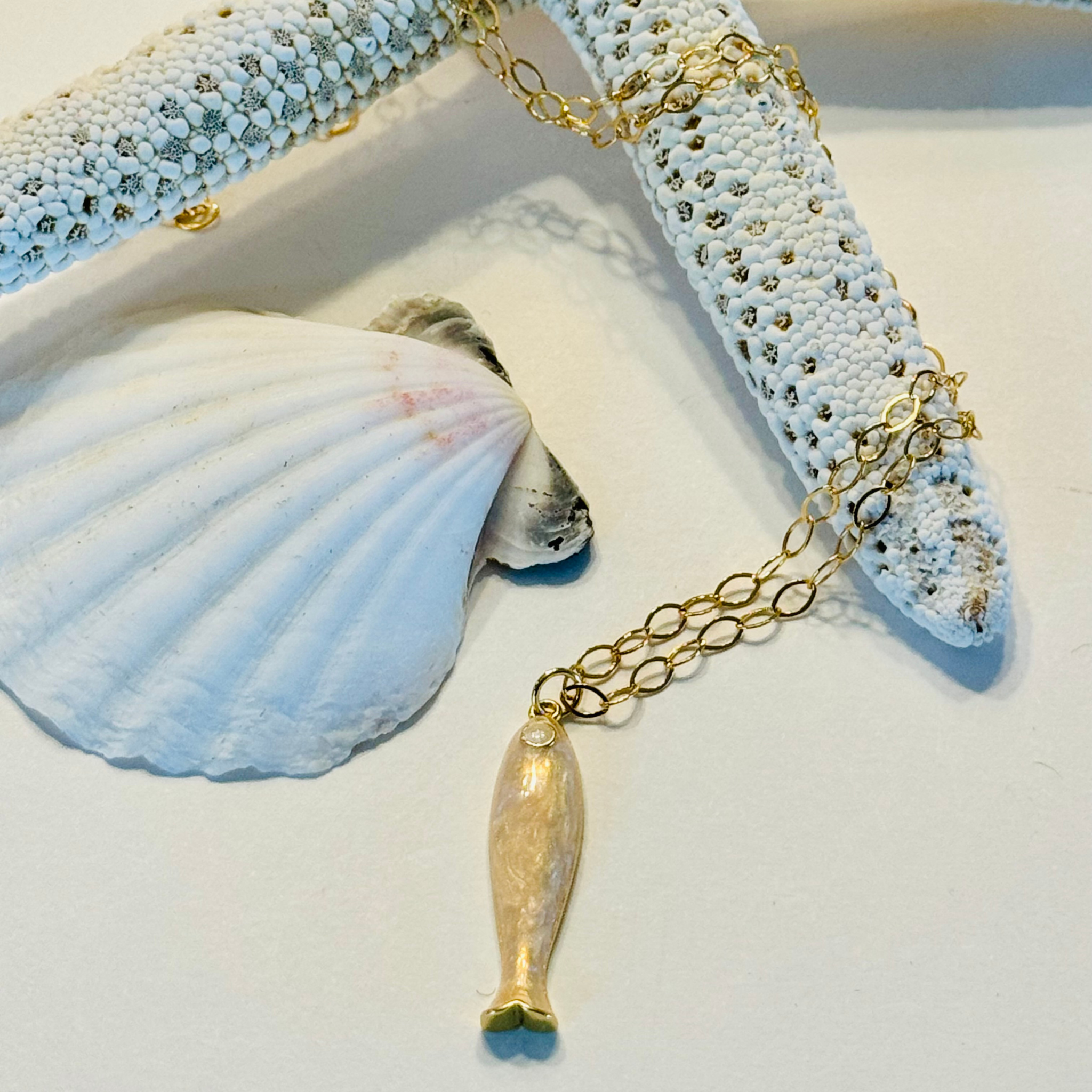 Gold necklace with a fish pendant on a white surface with shells.