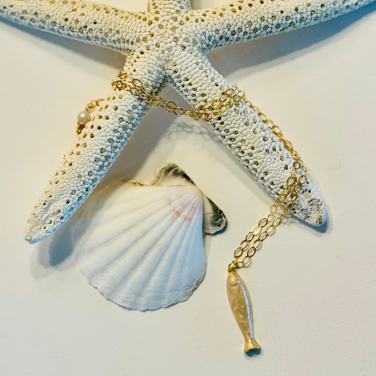 Gold chain necklace with a fish pendant on a starfish and shell background