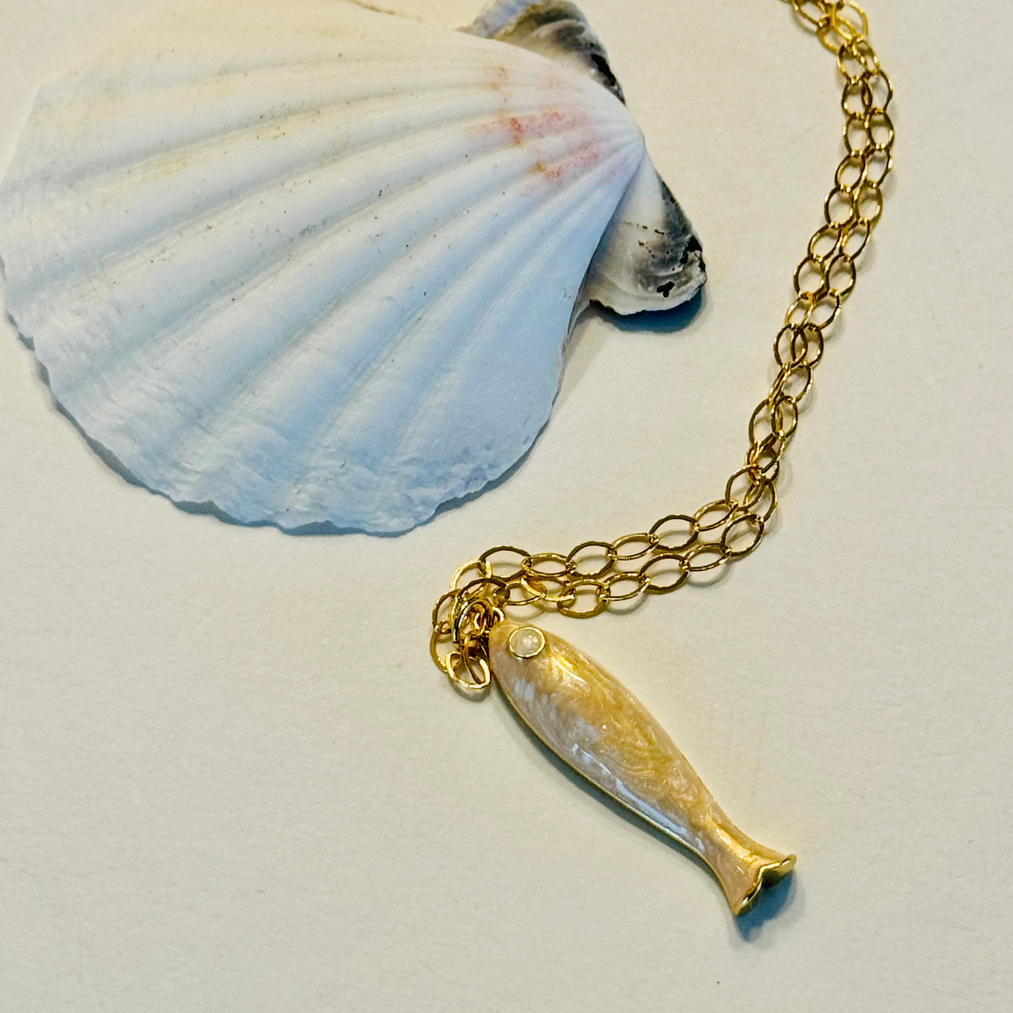 Gold fish pendant necklace on a white surface with a shell in the background