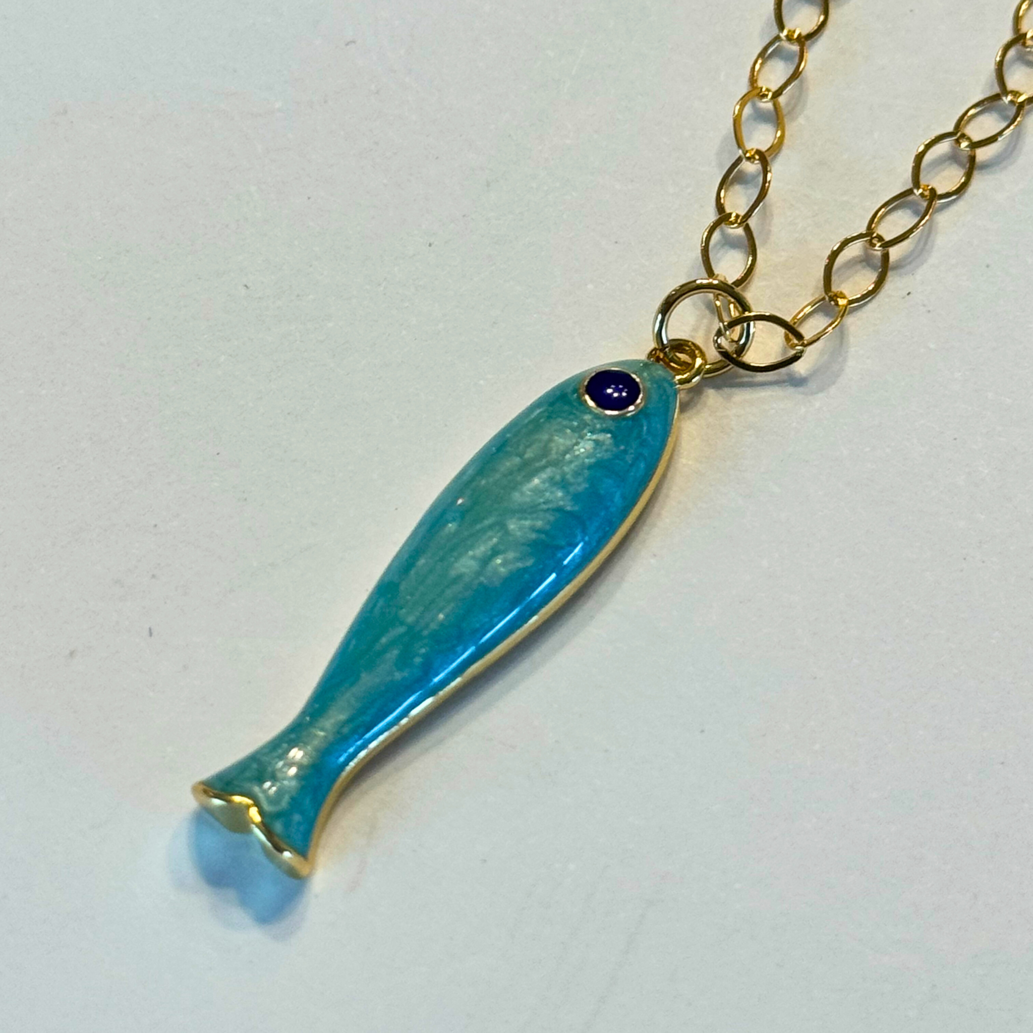 Turquoise fish-shaped pendant on a gold chain against a white background