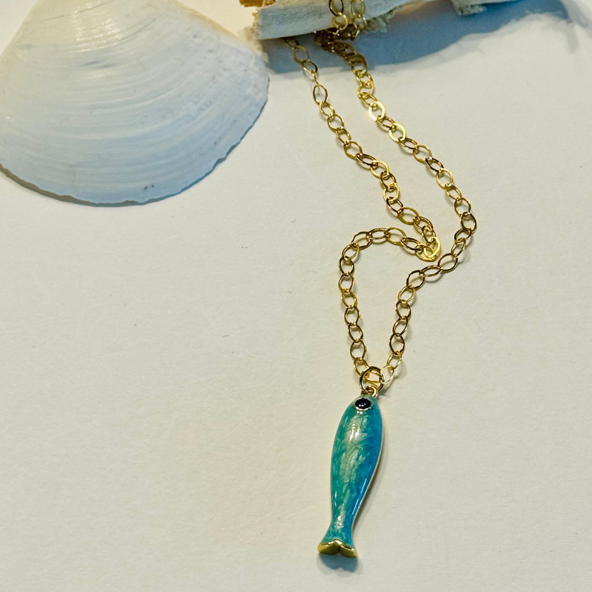 Gold chain necklace with a turquoise fish pendant on a light blue background