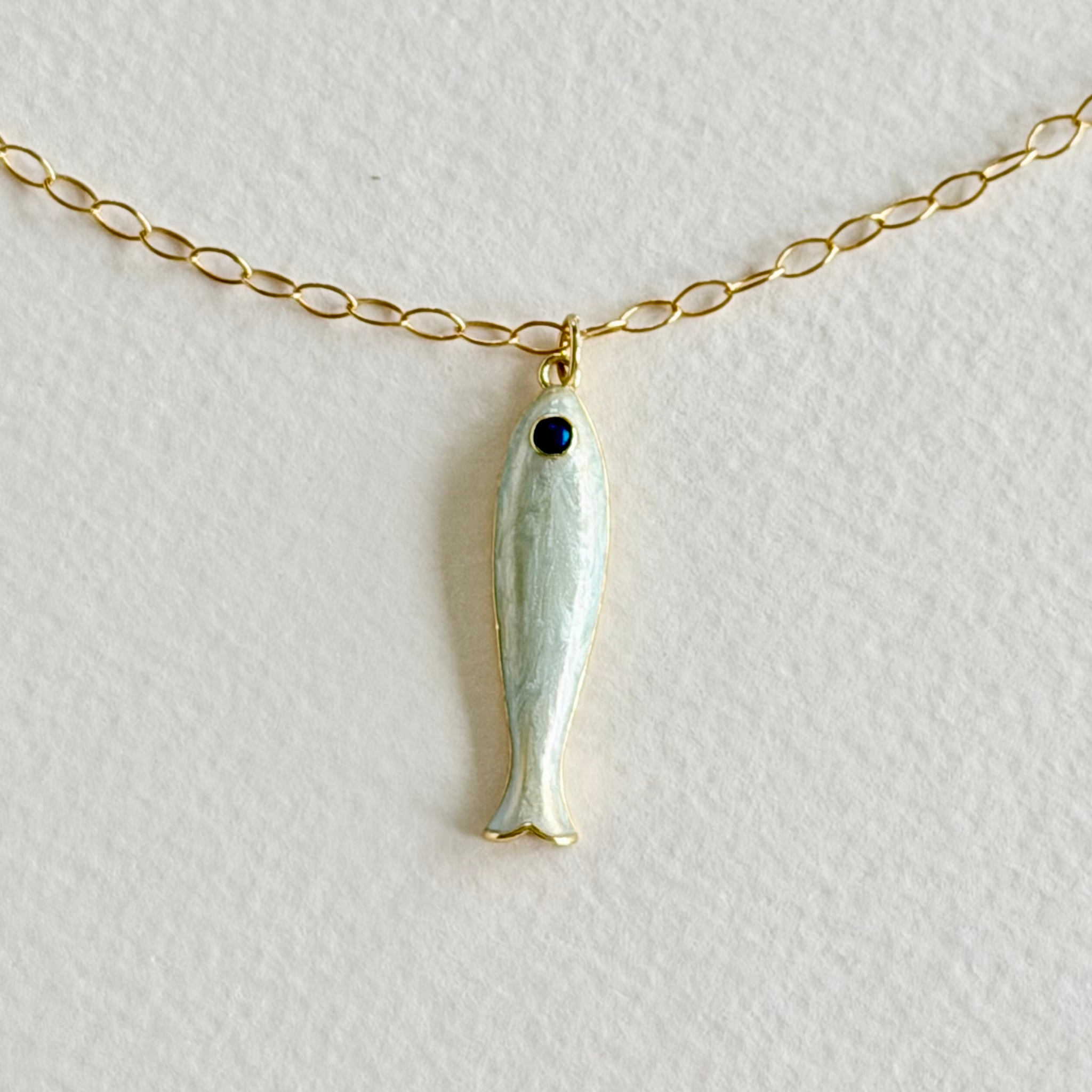 Gold necklace with a fish-shaped pendant on a light gray background